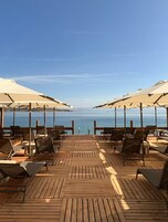 Terraza de madera con sillones de descanso y sombrillas con vistas a una masa de agua.