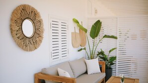 A living room with a wooden sofa, a round mirror, and two potted plants.