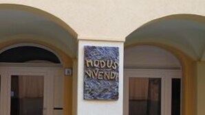 En byggnadsentré med två välvda dörröppningar och en skylt med texten ”MODUS NOVIDA”.