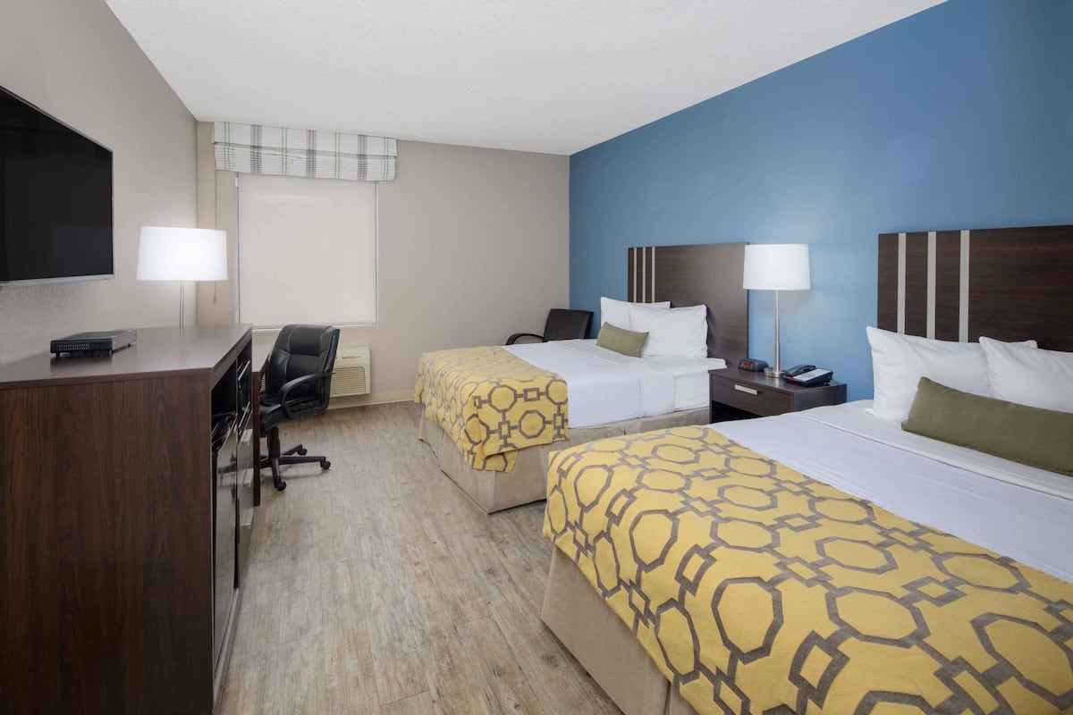 A hotel room with two beds, a desk, and a chair.