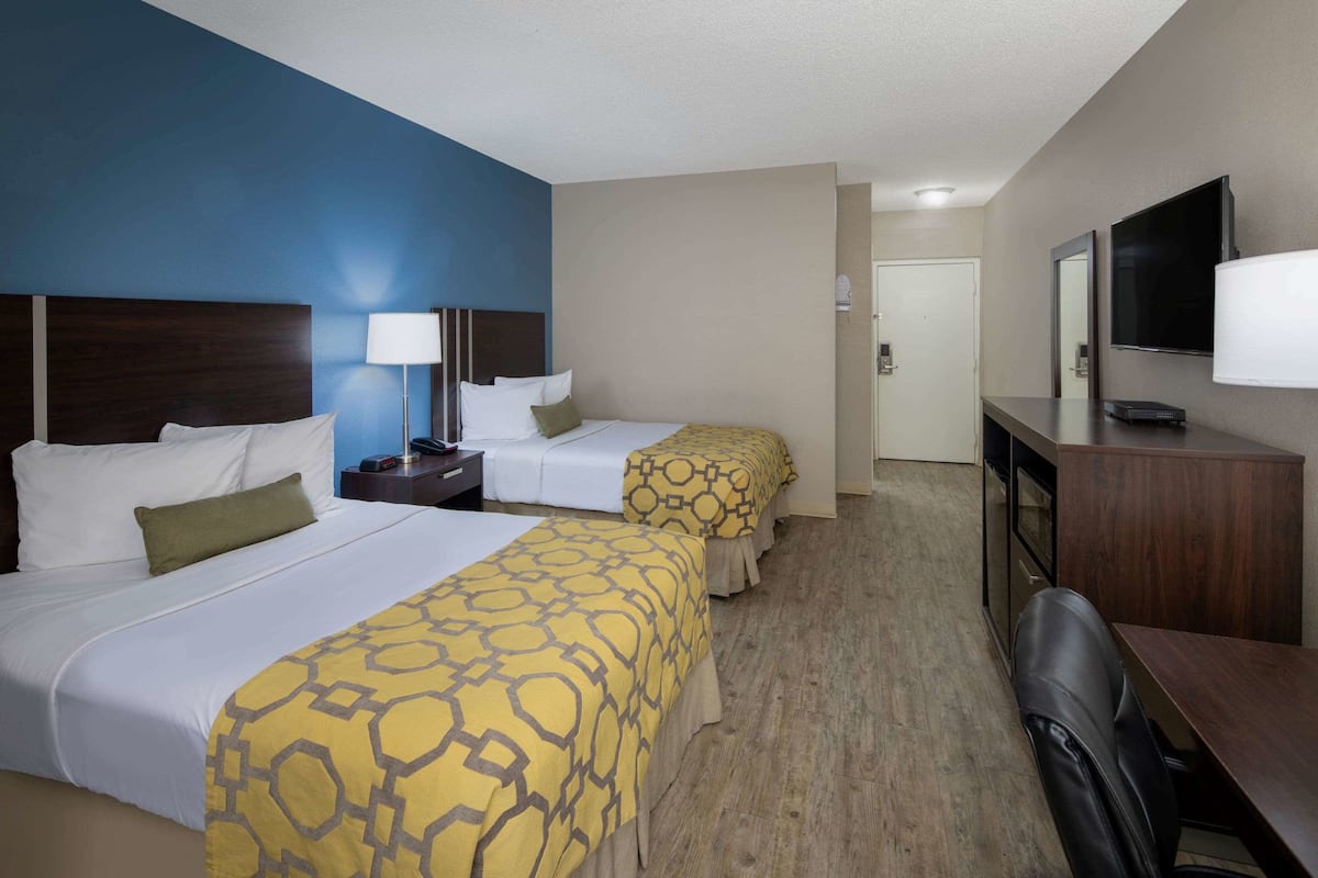 A hotel room with two beds, a desk, a chair, a TV, and a door leading to a bathroom.