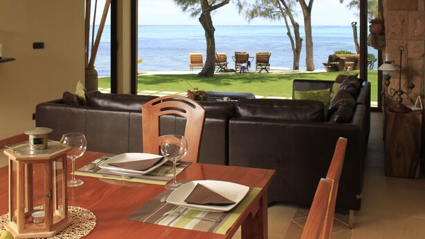 A dining area with a view of the sea, a wooden table set for two, and a leather sofa in the background. - Villa Fayette Sur Mer (Poste Lafayette)