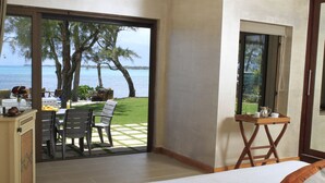 A bedroom with a large bed, a view of the sea through a sliding glass door, a small table with a tray, and a chair. - Villa Fayette Sur Mer (Poste Lafayette)