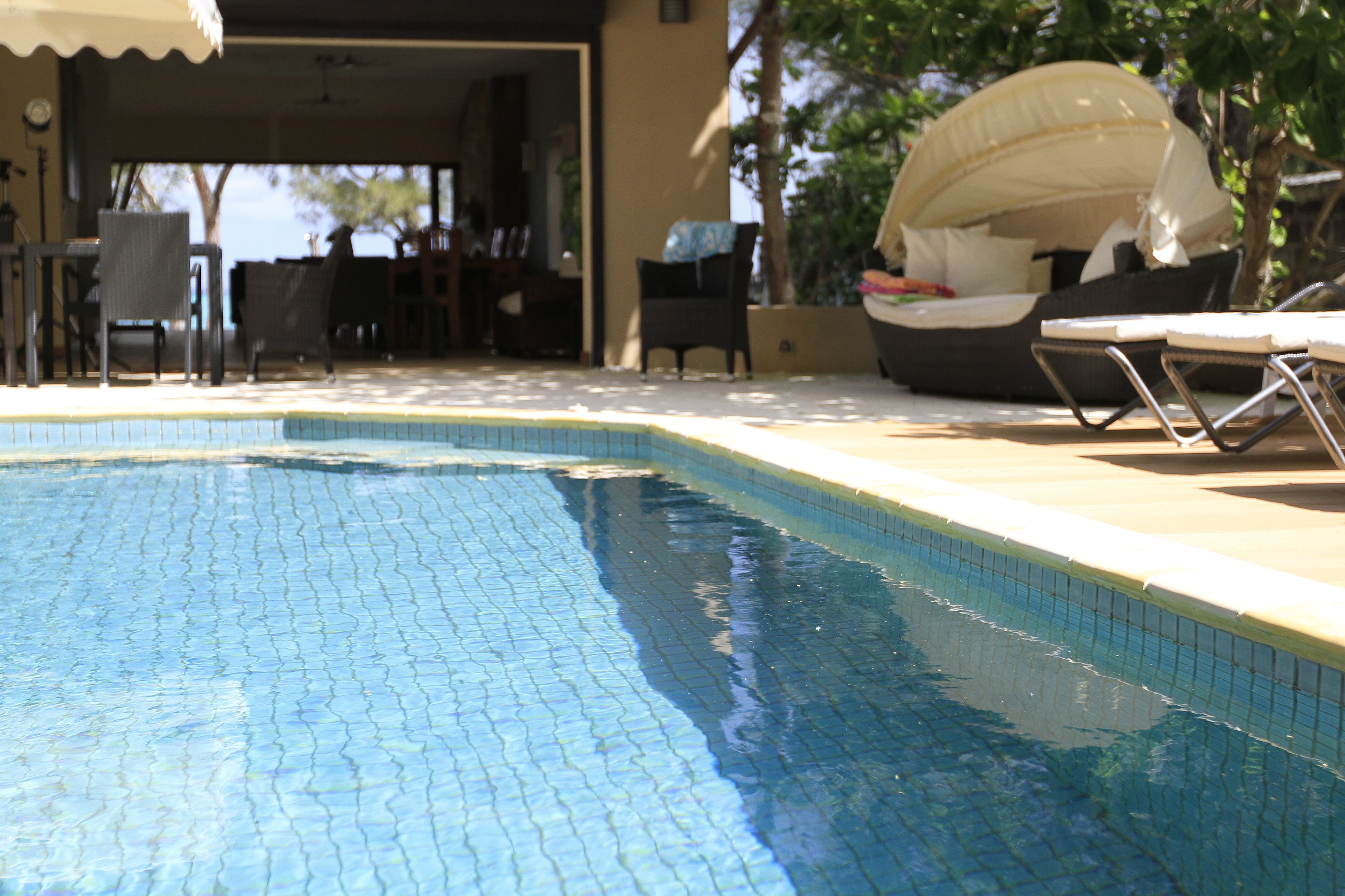 A swimming pool with tiled edges, lounge chairs, and a covered seating area.