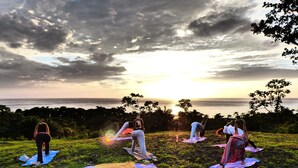 A group of people practicing yoga on mats in an outdoor setting with a view of the ocean at sunset. - Richmond Vale Diving and Hiking Center - Hostel (Chateaubelair)