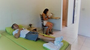 Ein Mann liegt auf einem grünen Sofa in einem Raum, in dem eine Frau an einem Schreibtisch sitzt.