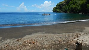A beach with a boat carrying passengers, clear blue water, and a forested hill in the background. - Richmond Vale Diving and Hiking Center - Hostel (Chateaubelair)