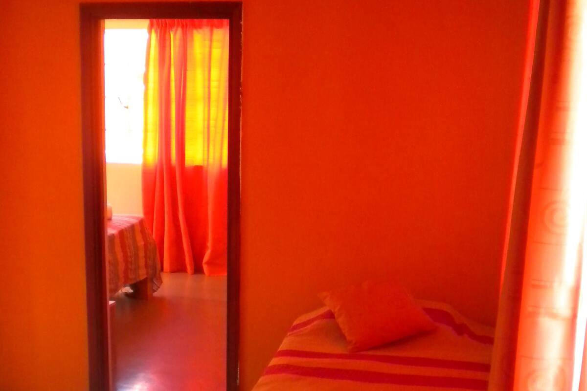 A room with orange walls, a bed with a striped bedspread, and a window with orange curtains.