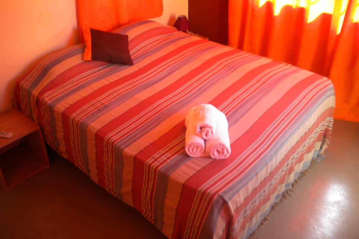 A bed with a striped bedspread, a pillow, and a rolled towel on it.