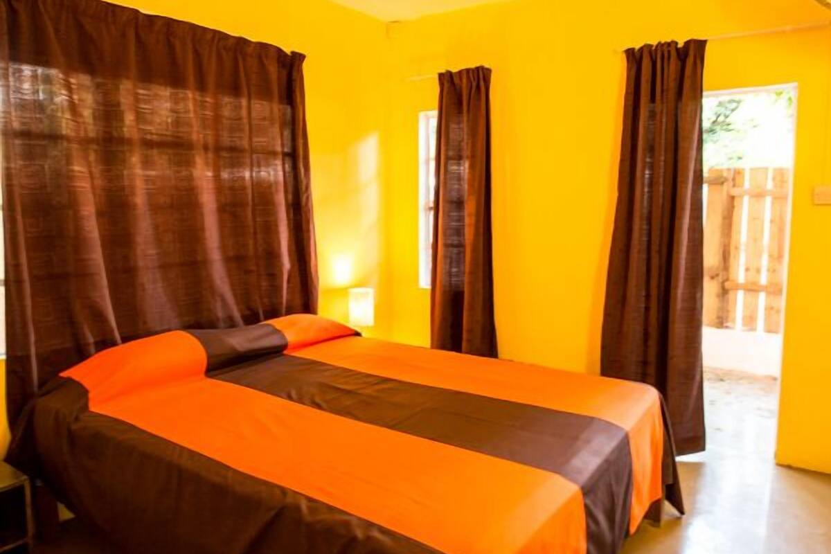 A room with two beds, each with an orange bedspread and brown curtains.