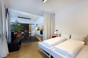 Quarto de hotel moderno com duas camas, uma escrivaninha, uma cadeira, uma mesinha e um vaso de planta.