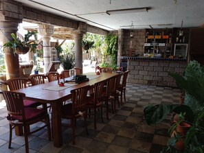 A restaurant with a long wooden table and chairs, surrounded by potted plants and a stone wall.