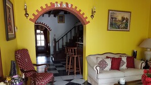 Een kamer met een zwart-wit geruite vloer, een bank, een stoel, een tafel en een trap die naar een andere kamer leidt.