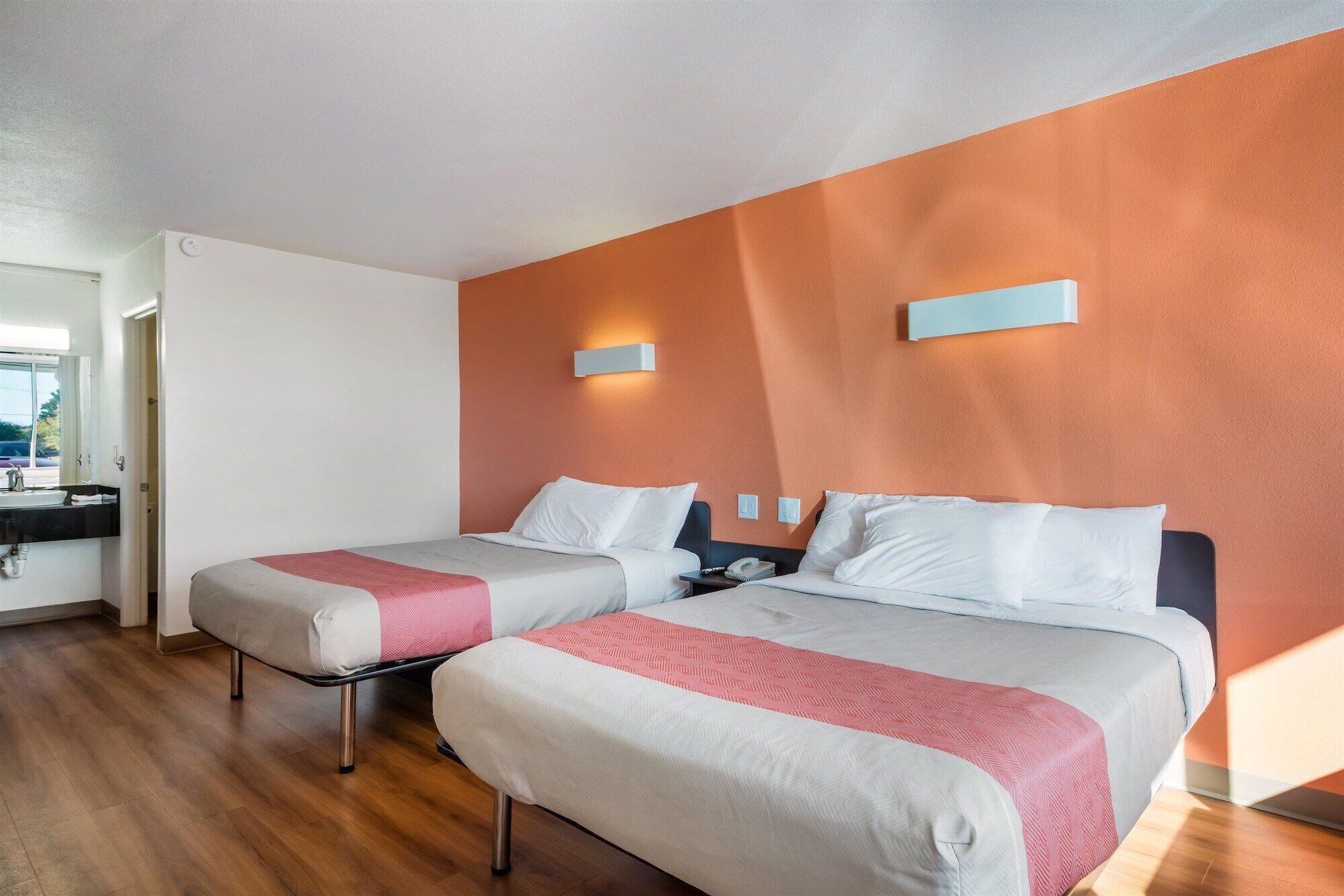 A hotel room with two beds, a bathroom, and a view of the outside.