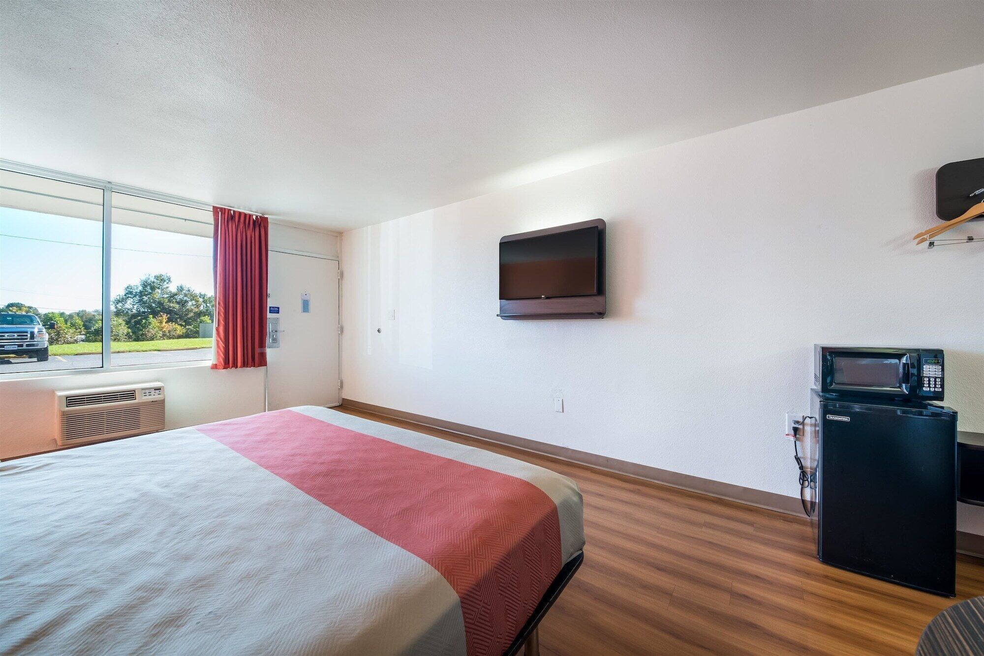 A hotel room with a bed, a television mounted on the wall, a microwave, and a window with a view of the outside.