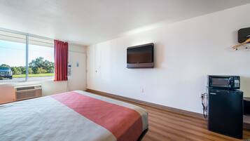 A hotel room with a bed, a television mounted on the wall, a microwave, and a window with a view of the outside.