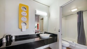 A bathroom with a black countertop, a white sink, a mirror, and a shower area. - Motel 6 Connellys Springs, NC (Icard)