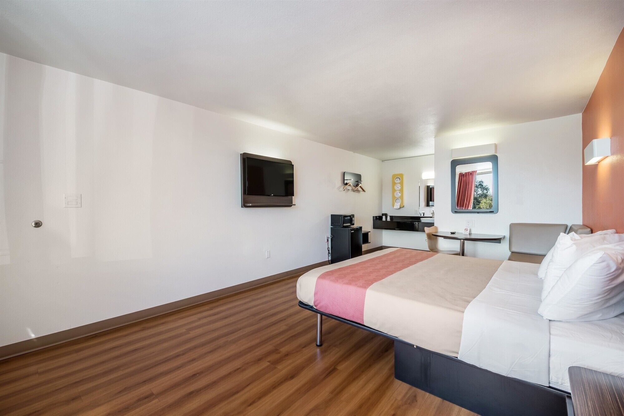 A hotel room with a bed, a desk, a TV, a microwave, and a small kitchenette.