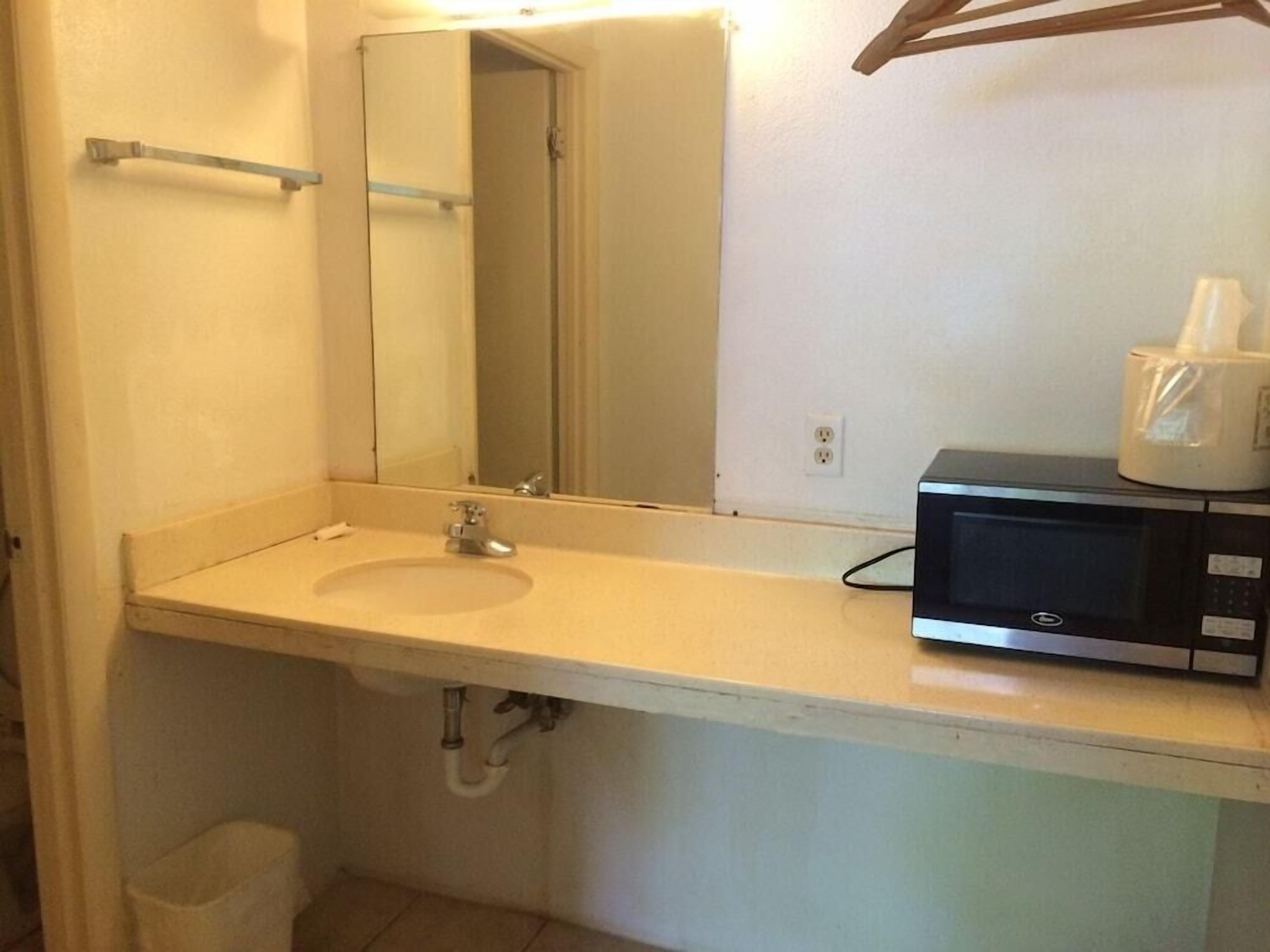 Un baño con lavamanos, espejo y un microondas en la encimera.