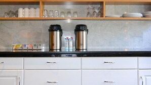 A kitchen with white cabinets, a black countertop, and a cityscape painting above. - Hotel Bienvenue (Rotterdam)