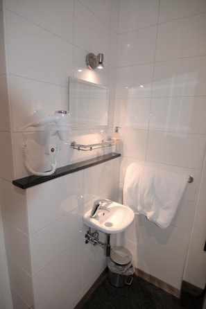 A small bathroom with a white sink, a mirror, a towel rack, and a hairdryer on a shelf. - Hotel Bienvenue (Rotterdam)