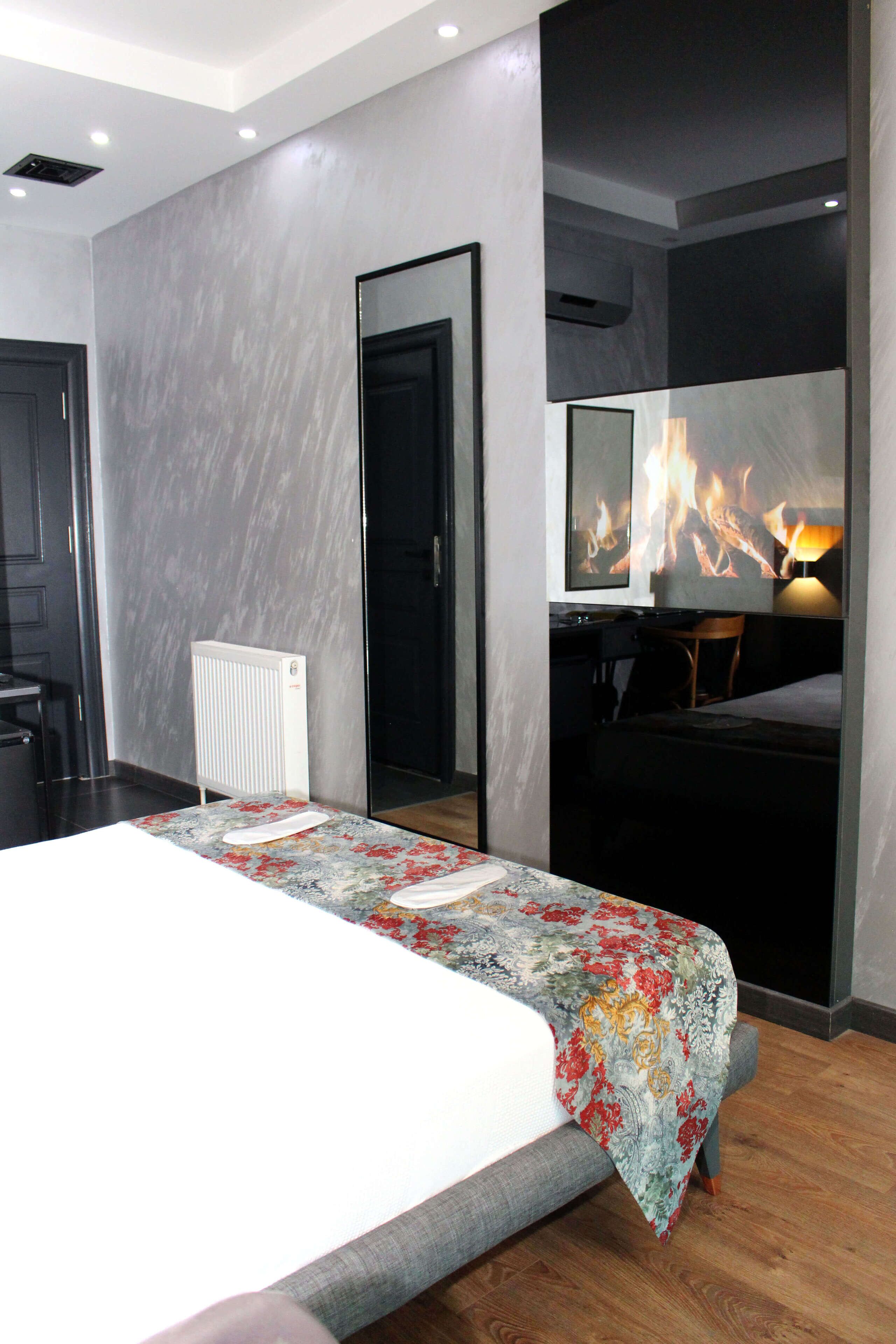 A modern hotel room with a large bed, a flat-screen TV mounted on the wall, a radiator, and a desk with a chair.