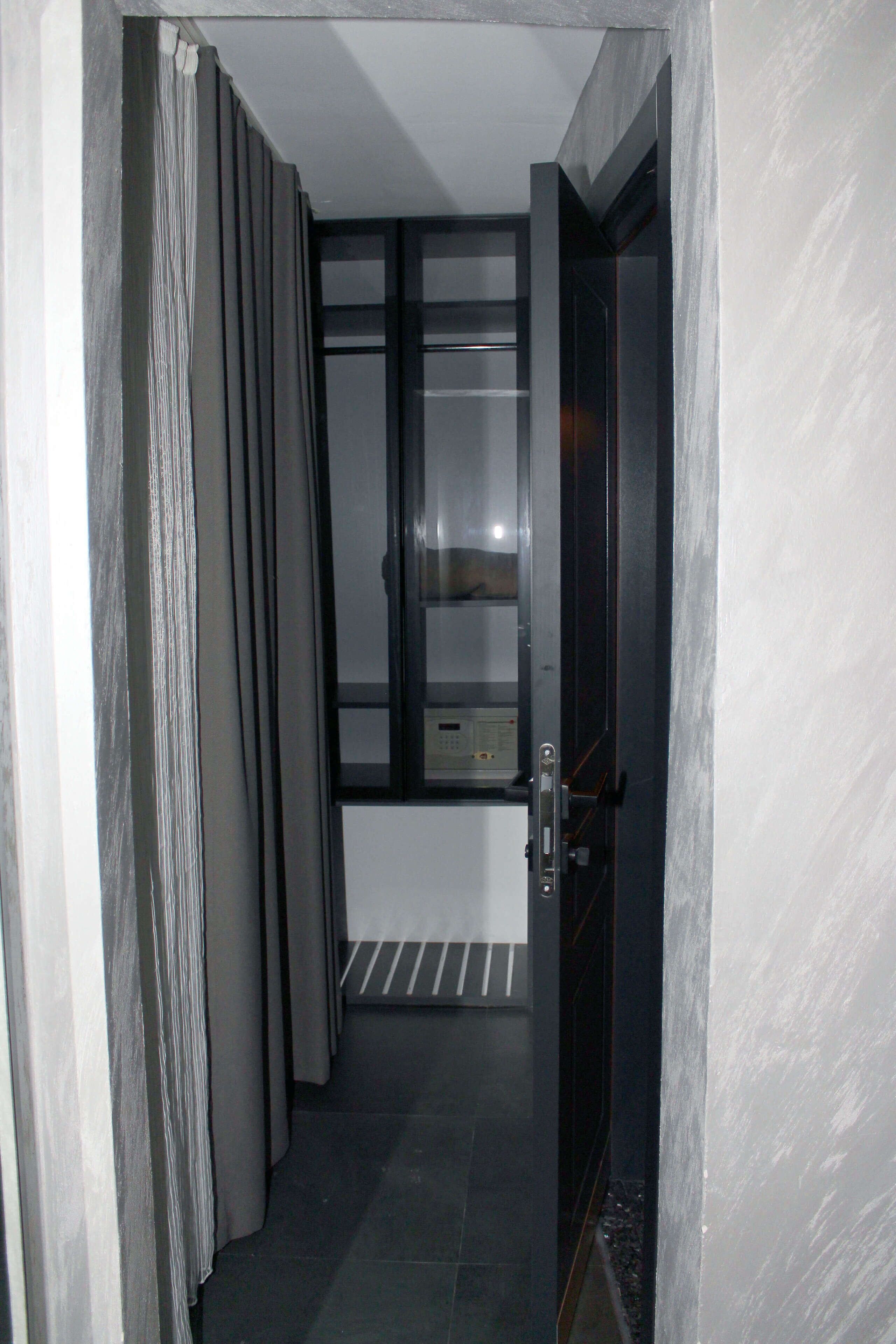 A narrow hallway with a door leading to a room with a window and a control panel.