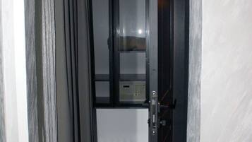 A narrow hallway with a door leading to a room with a window and a control panel.