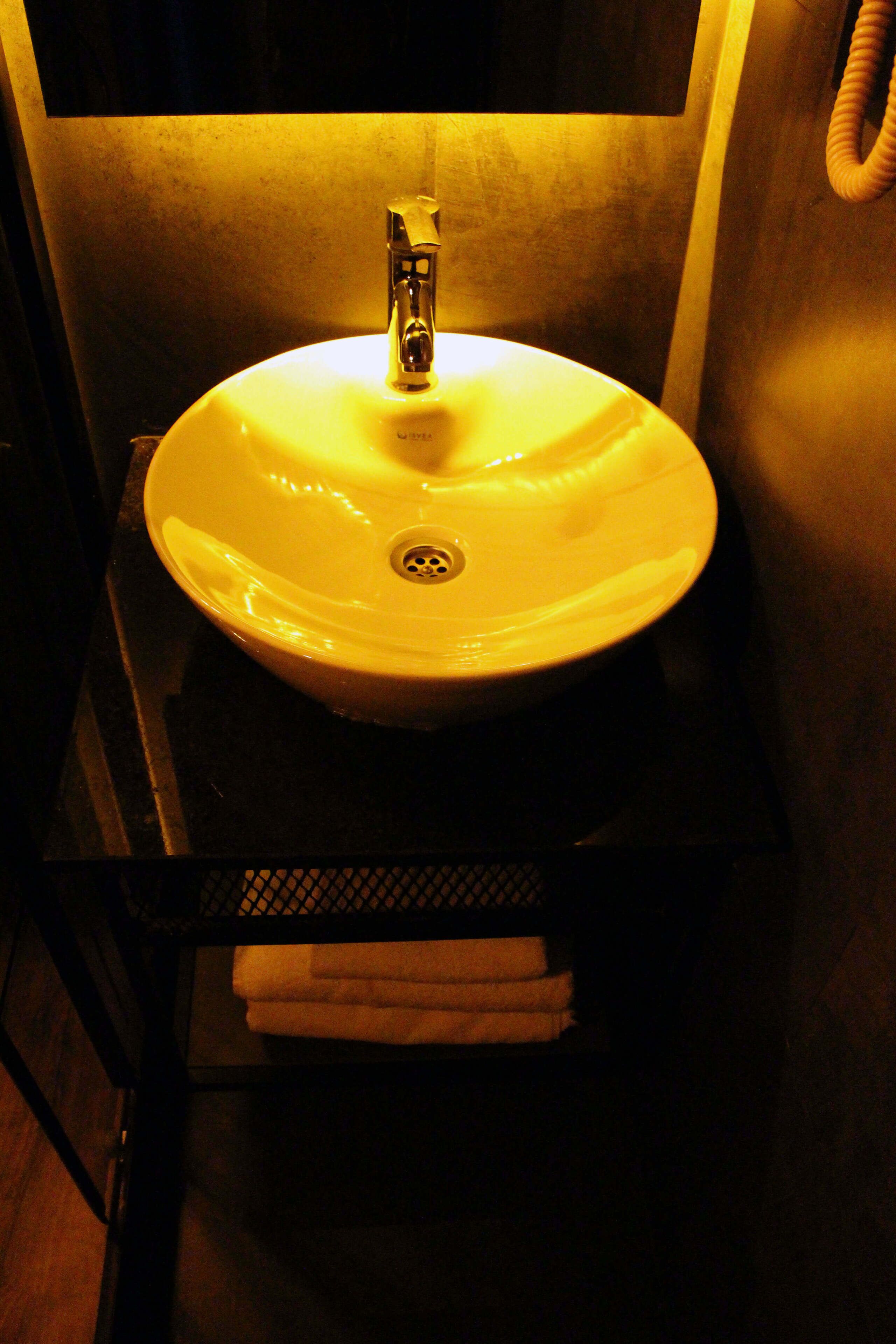 Een badkamer met een witte wastafel, een kraan en een handdoekrek met handdoeken.