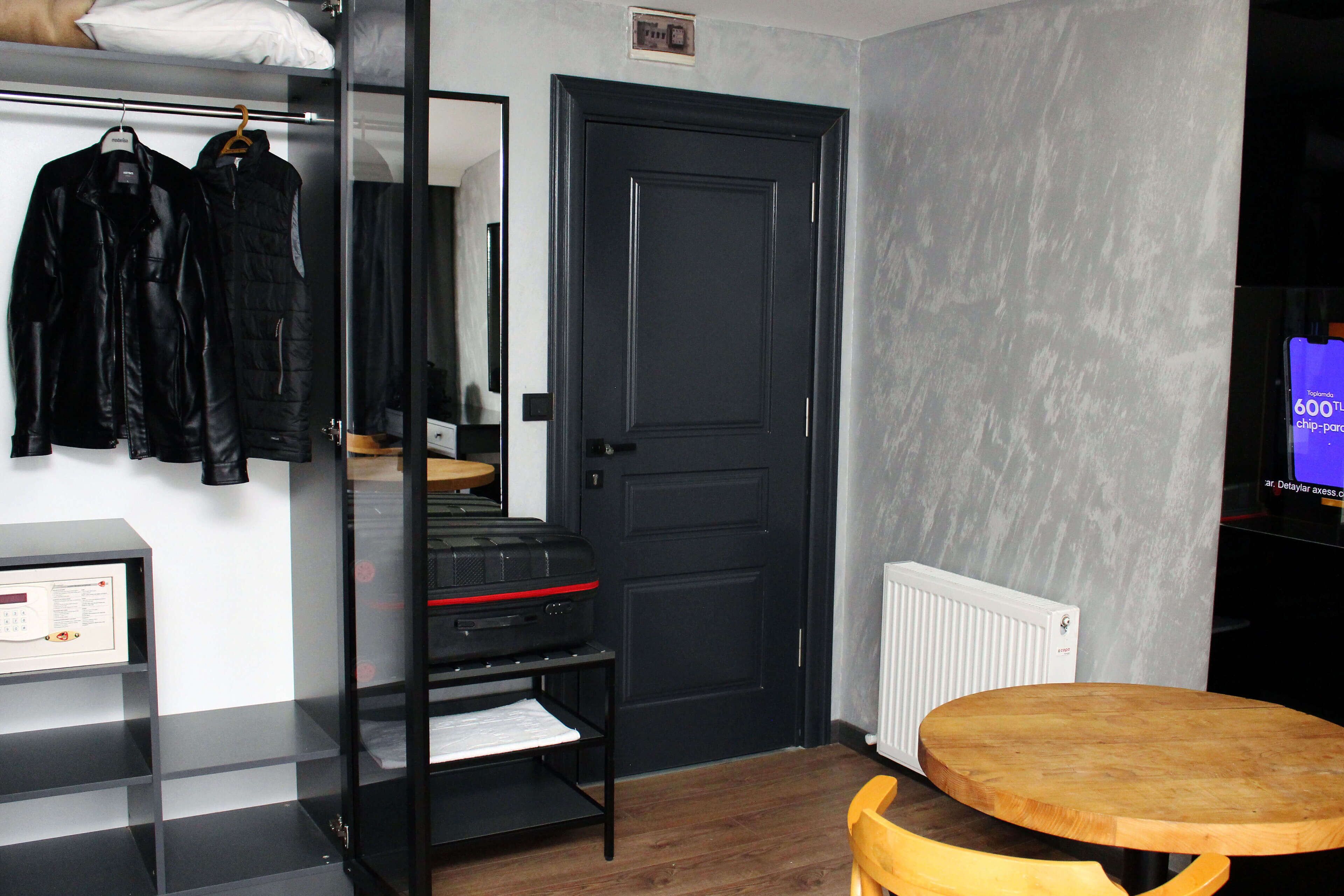 Una habitación con una puerta negra, una mesa de madera y un estante con chaquetas.
