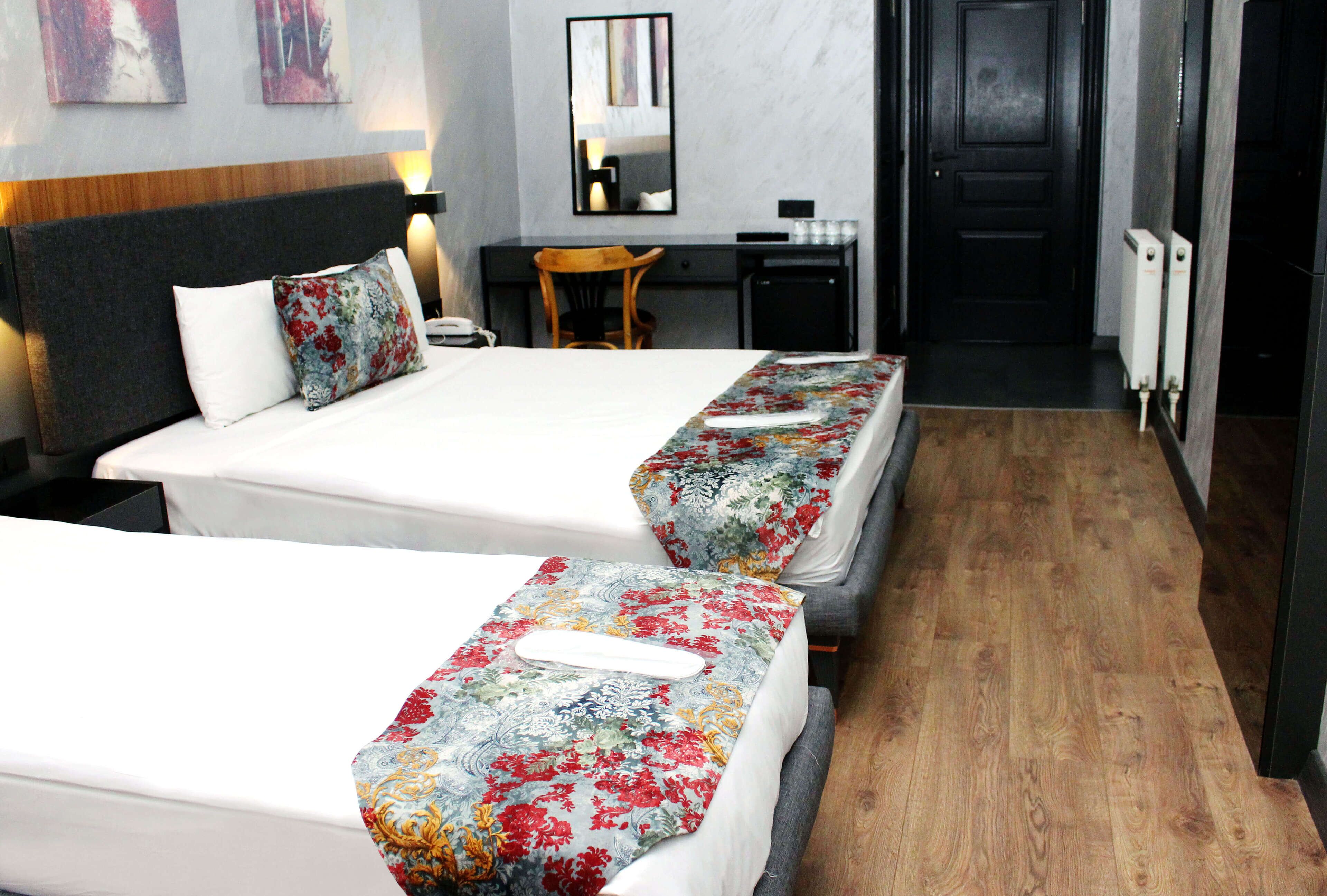 A hotel room with two beds, a desk, a chair, and a door.
