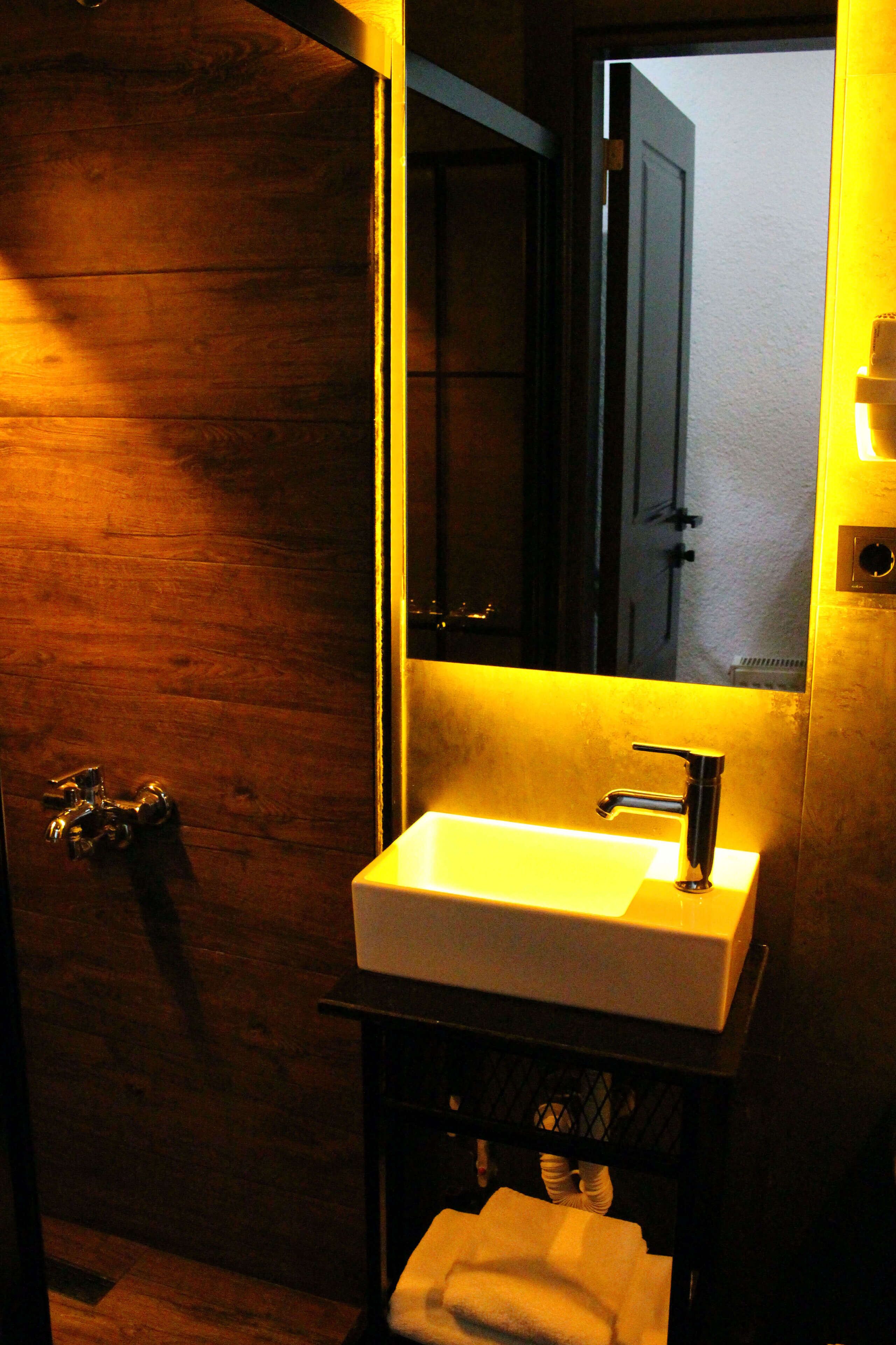 Une salle de bain avec une porte en bois, un lavabo blanc et un miroir.