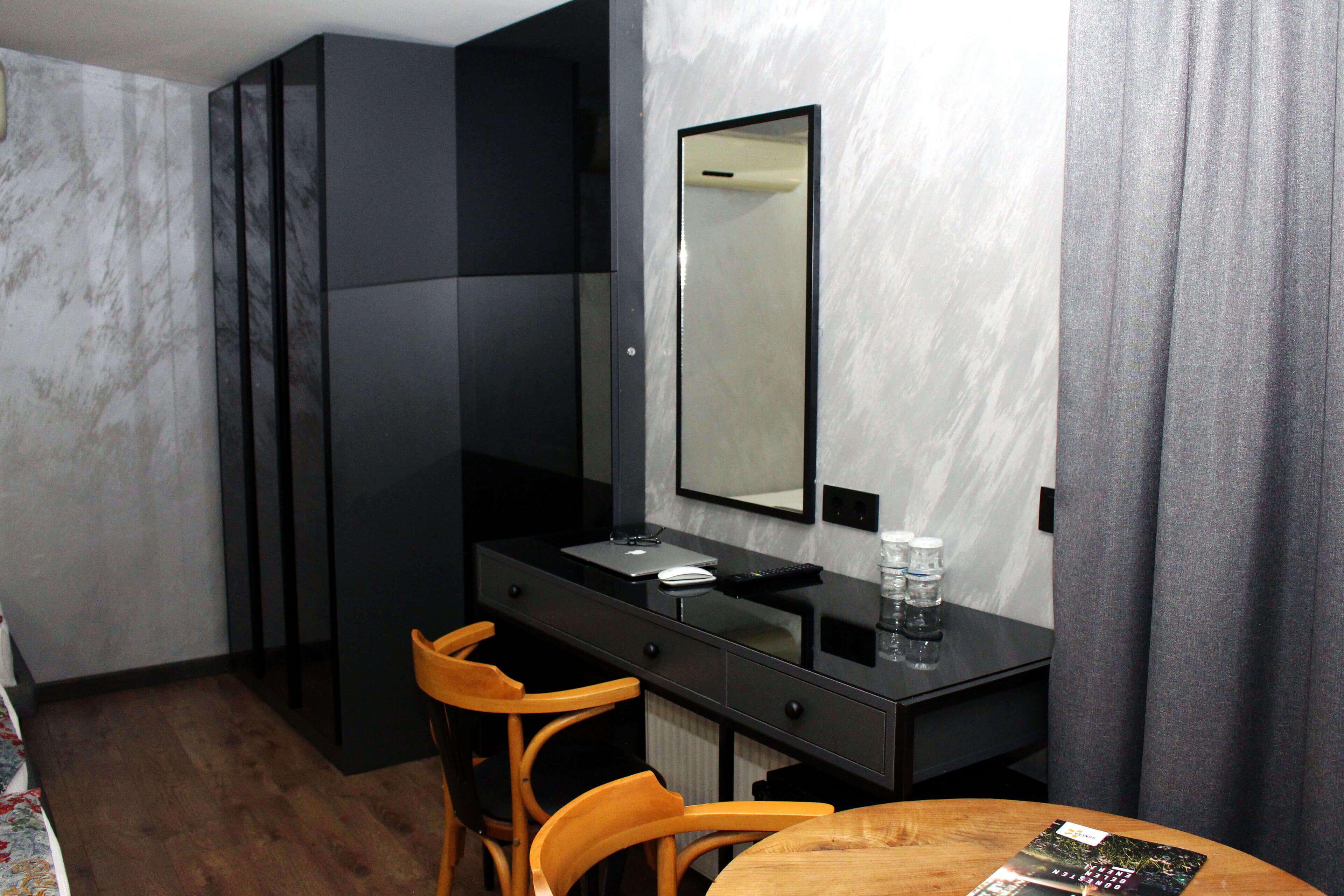 Una habitación de hotel moderna con una mesa de comedor de madera, un escritorio negro con un espejo y una silla.