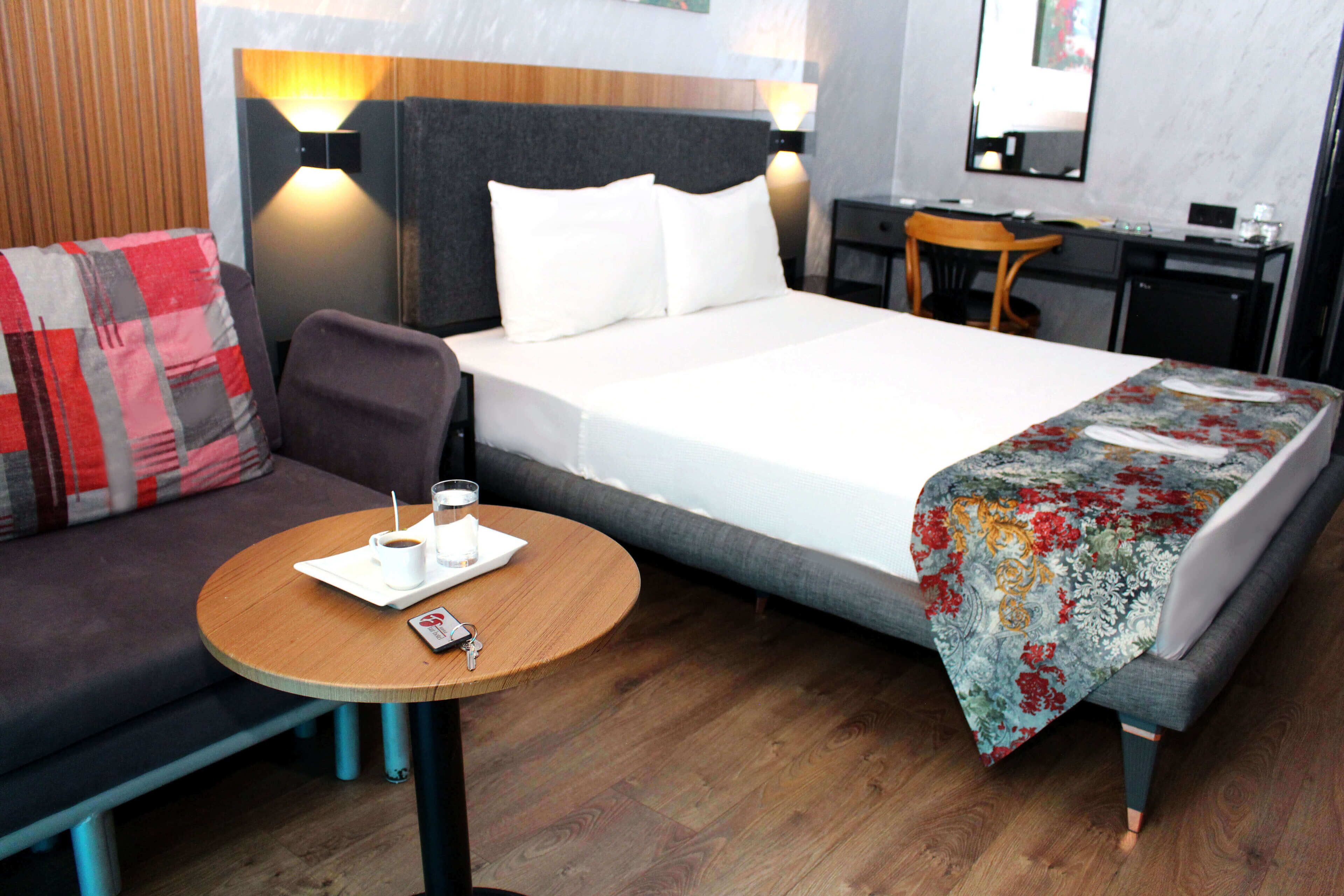 A hotel room with a bed, a sofa, a desk, and a small table with a cup and saucer.