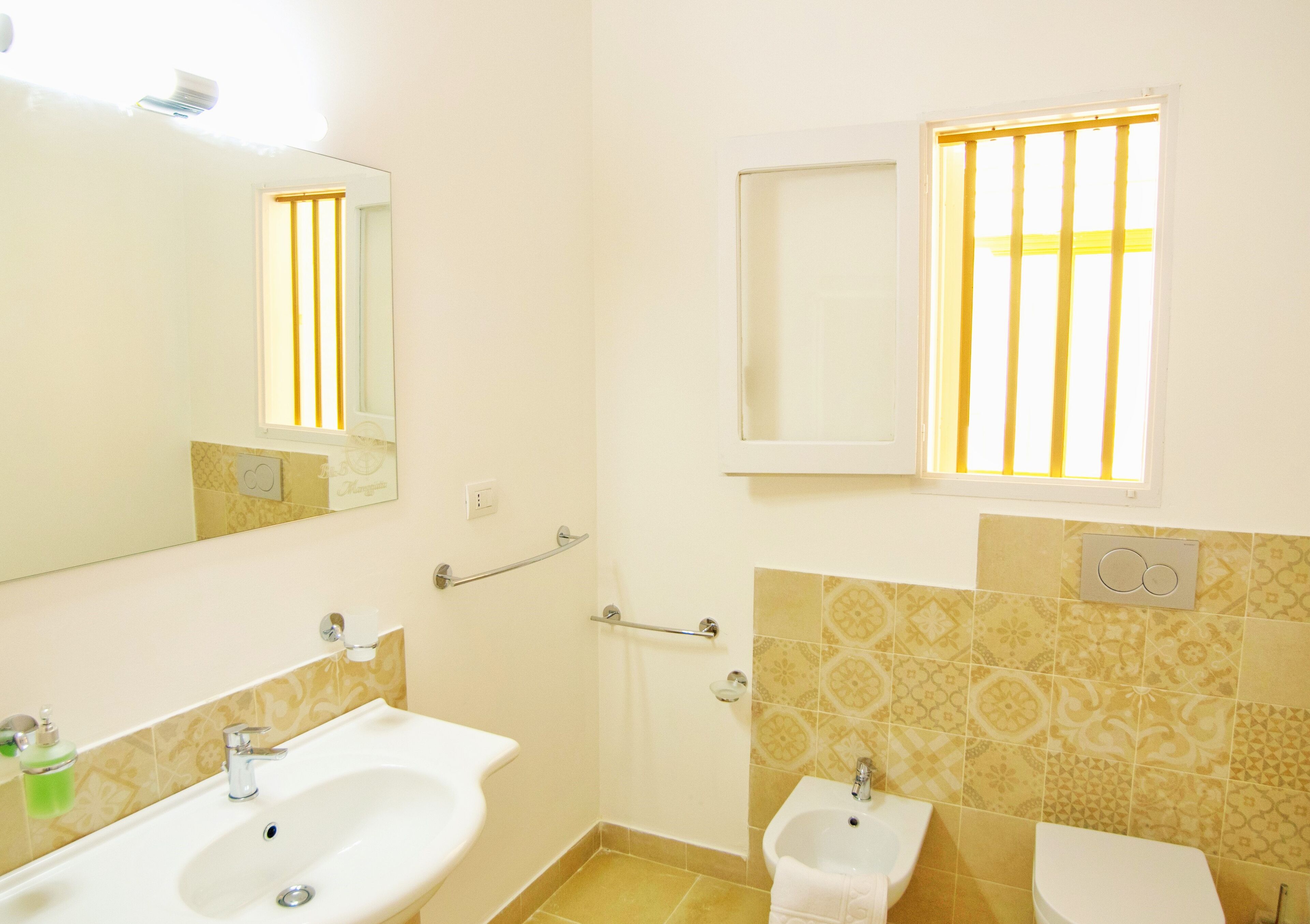 A bathroom with two sinks, a mirror, a window with bars, and patterned tiles.