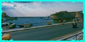 A coastal road with a stone wall on one side and a marina with boats on the other. - B&B Mareggiata (Gallipoli)