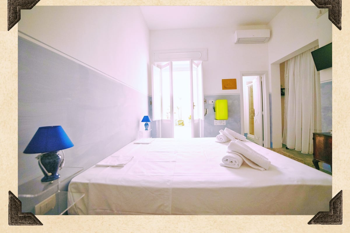A hotel room with a bed, a nightstand with a lamp, and a bathroom visible through an open door.