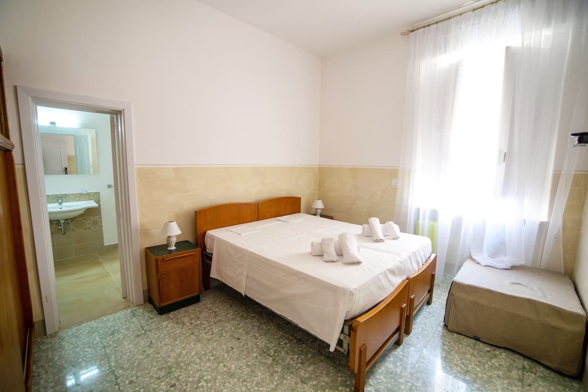 A hotel room with a bed, bedside table, lamp, and a bathroom visible through an open door.