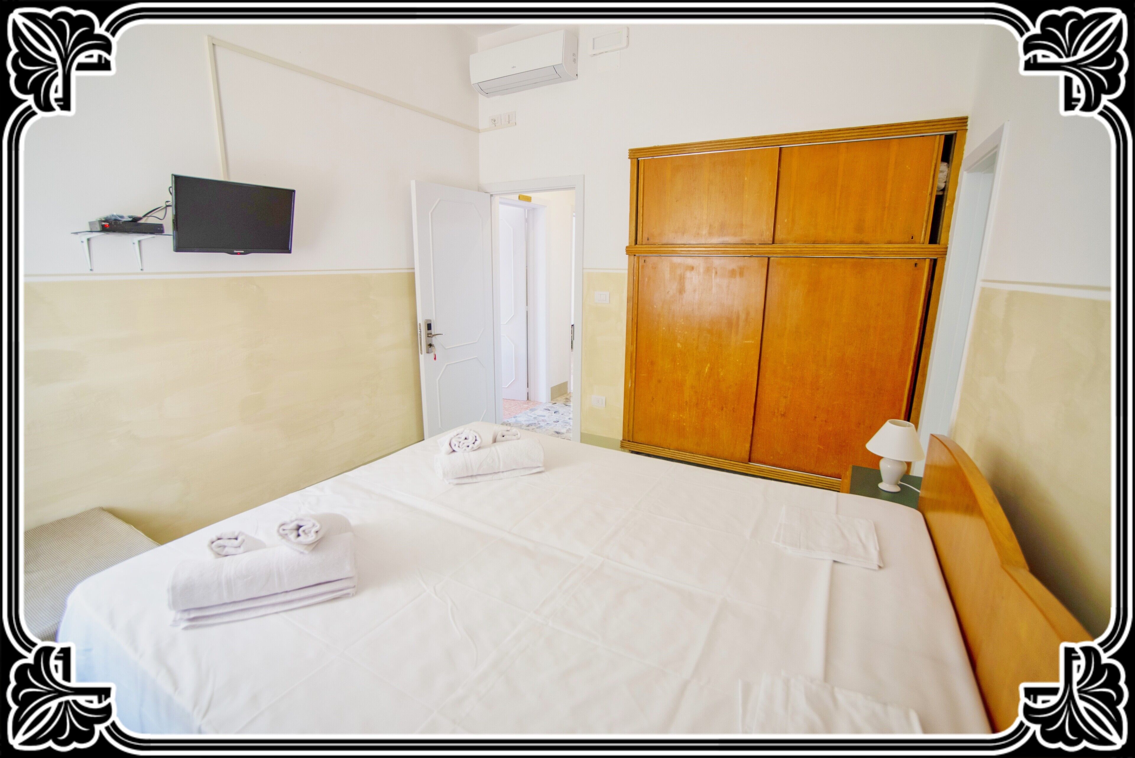 A hotel room with a bed, a wardrobe, a television, and a door leading to another room.