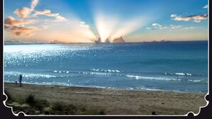 Una playa con cielo despejado y reflejos de sol en el agua.