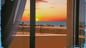 Vista del atardecer desde un balcón con playa y costa rocosa al fondo.