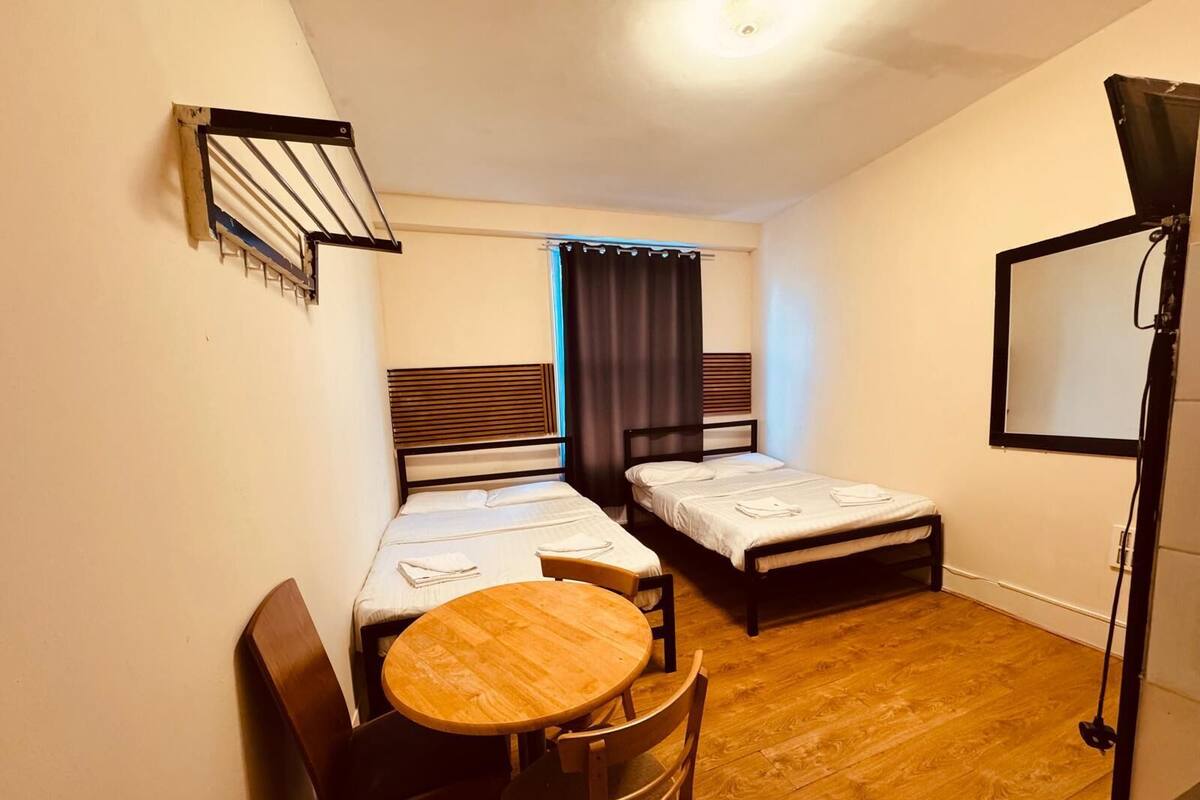 A small room with two single beds, a wooden table with chairs, and a TV mounted on the wall.
