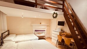 Une chambre avec deux lits, un escalier en bois, une cheminée et un bureau avec des chaises.