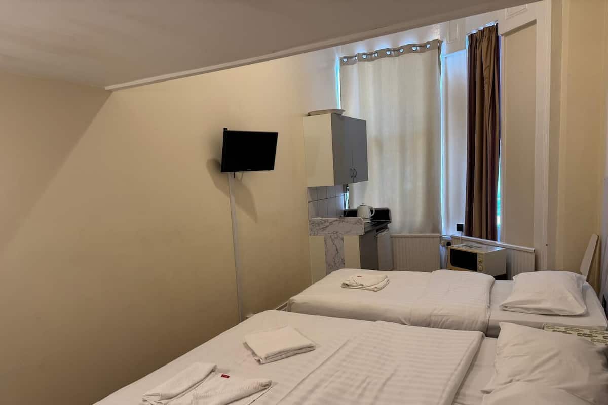 A hotel room with two beds, a TV, a small kitchenette, and a window with curtains.