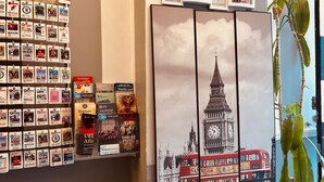 Un mur orné d’affiches de voyage, un tableau représentant une tour de l’horloge et une plante.
