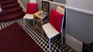 Un escalier recouvert d’une moquette rouge, un sol à carreaux et un miroir qui reflète un tableau et un lustre.