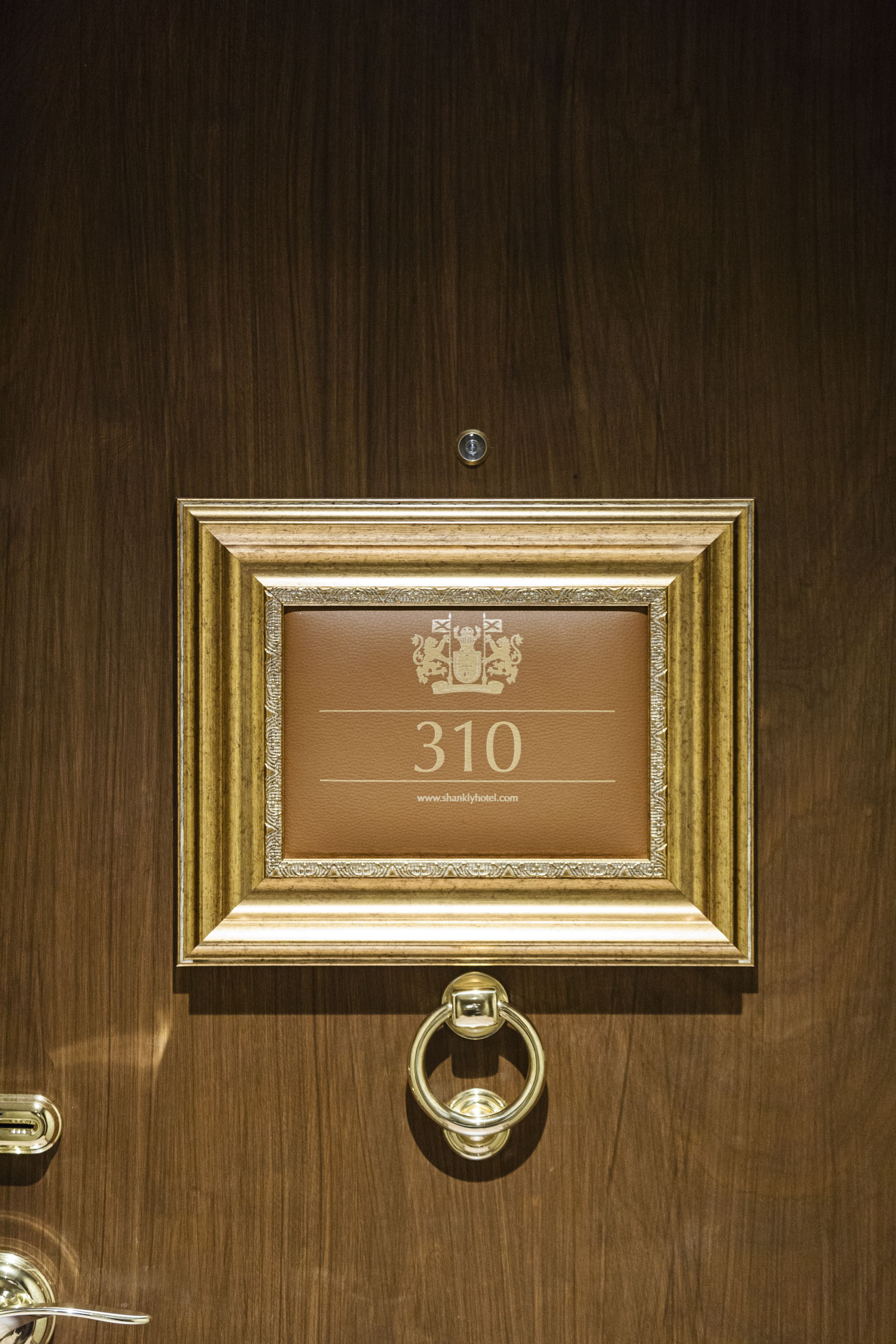 A wooden door with a gold-framed plaque displaying the number 310 and a website URL.