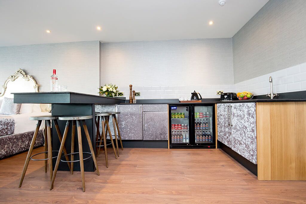 Uma cozinha moderna com área de bar, geladeira abastecida com bebidas e um espaço de estar com sofá e banquetas.