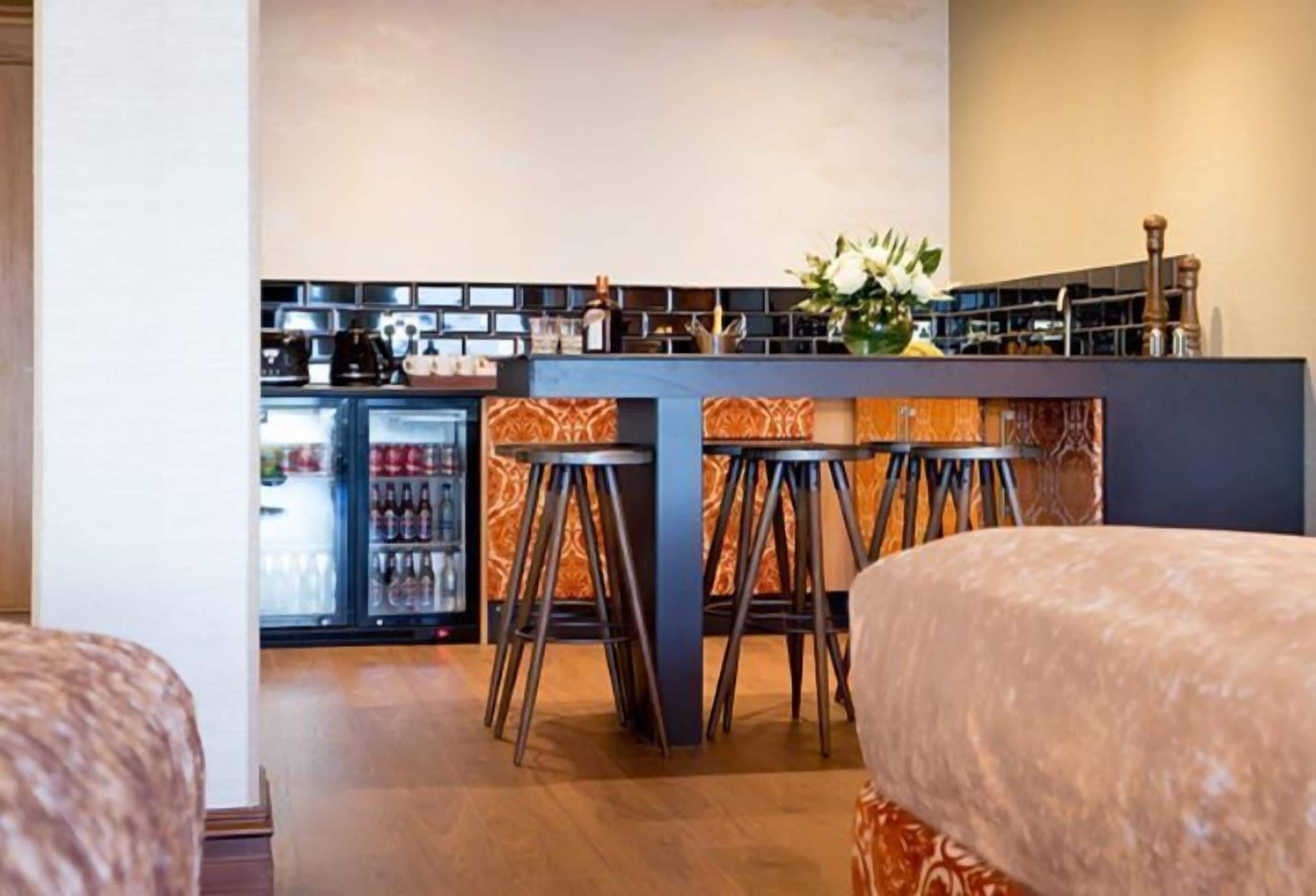 A bar area with stools, a refrigerator stocked with beverages, and a decorative vase.