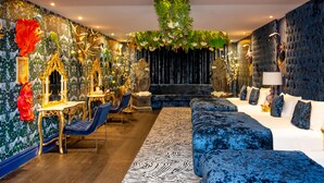 A luxurious room with a plush blue sofa, a wooden floor, and a decorative wall with a floral arrangement.